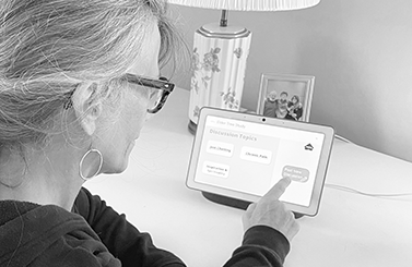 An older adult points to the screen of a smart display.